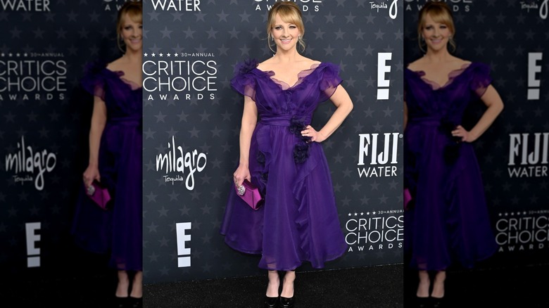 Melissa Rauch on the red carpet in a purple dress with ruffles, flowers, and layers of organza