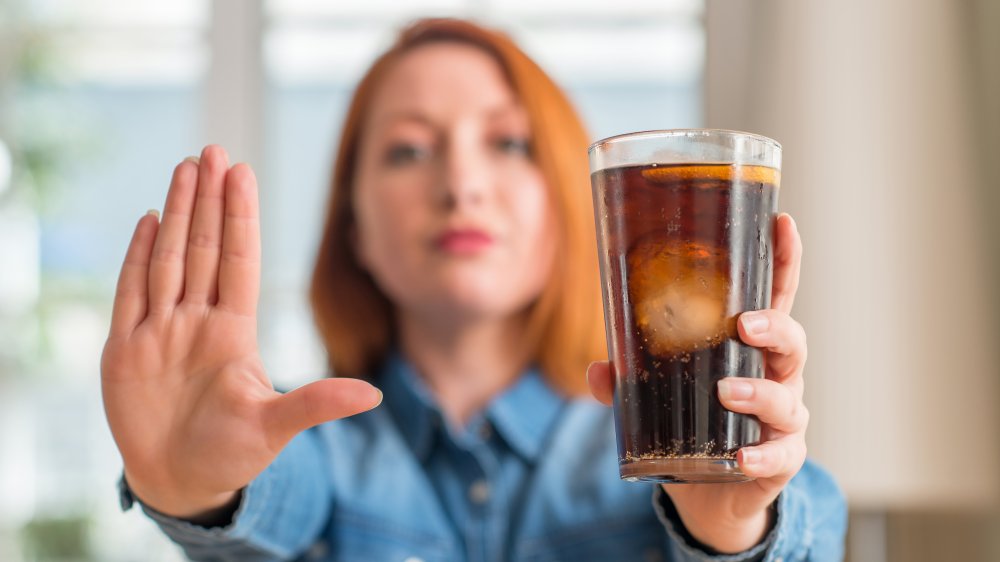 A woman holding a glass of soda, a beverage you should avoid while pregnant
