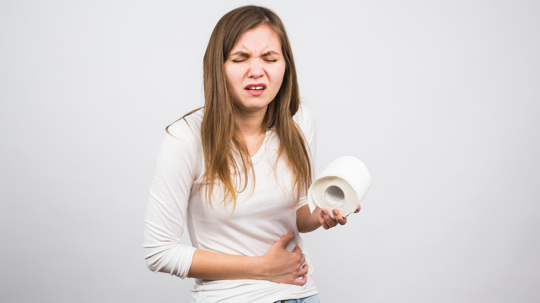 woman clutching stomach in pain holding a roll of toilet paper