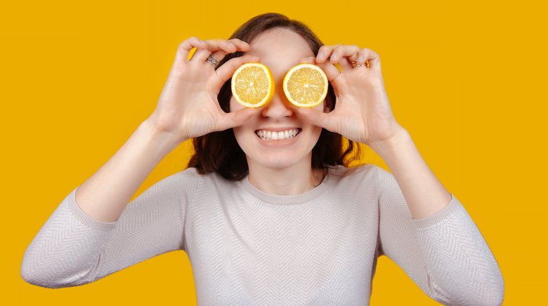 woman holding lemon halves in front of eyes