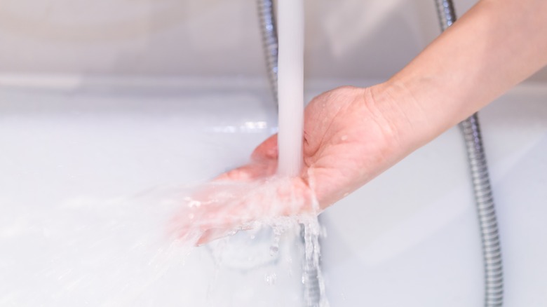 woman holding hand under bath tap