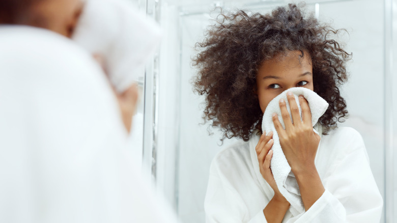 woman drying her face while looking in the bathroom mirror