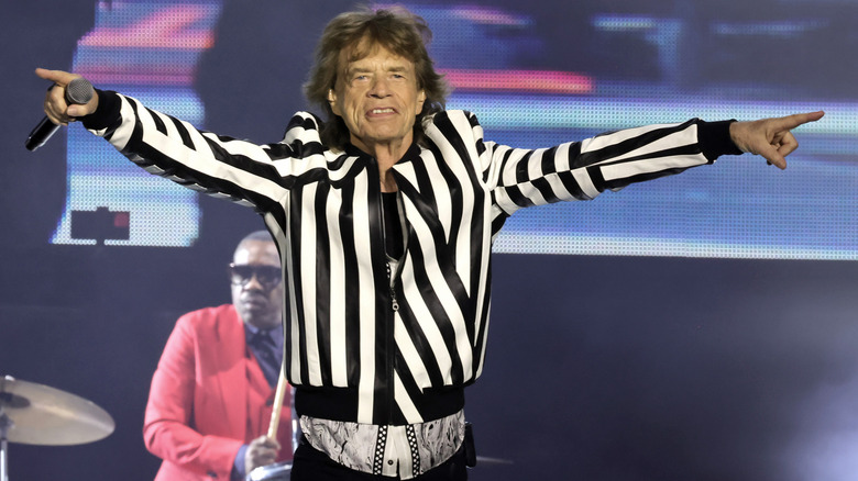 Mick Jagger holding microphone pointing with both hands on stage