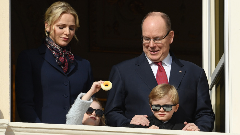 Princess Charlene looking down at her daughter and Prince Albert smiling with his hands on his son's shoulders