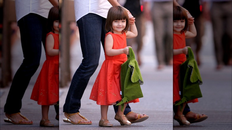 Suri Cruise smiles while holding a woman's hand 