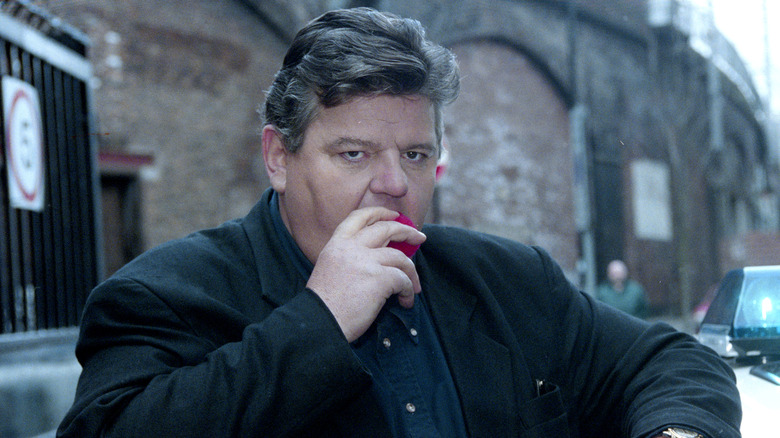 Robbie Coltrane eating an apple in black coat 