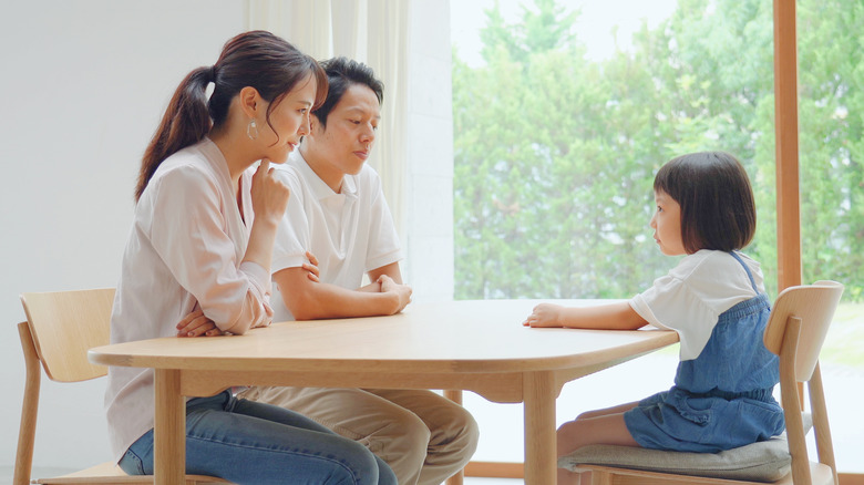 Asian mother and father sitting with young daughter at table