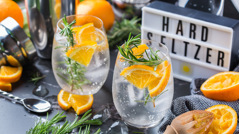 Sparkling orange and mint cocktail in a glass, sign reads "hard seltzer" behind