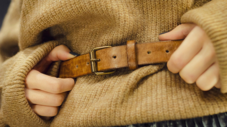 A woman's hands holding the belt at her waist