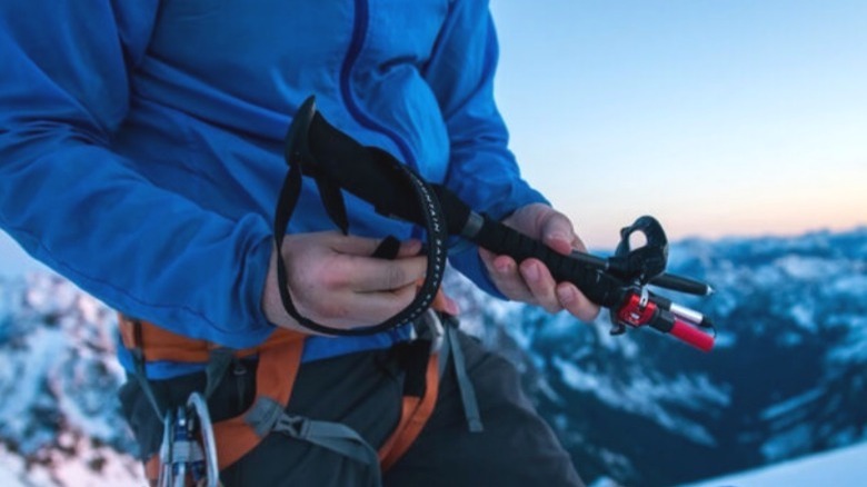 Hiker in blue coat holding folded trekking poles