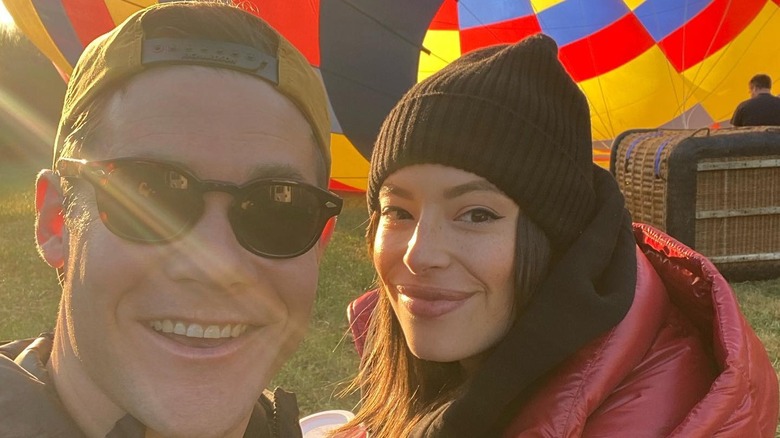 Adam and Chloe smile in front of a hot air balloon