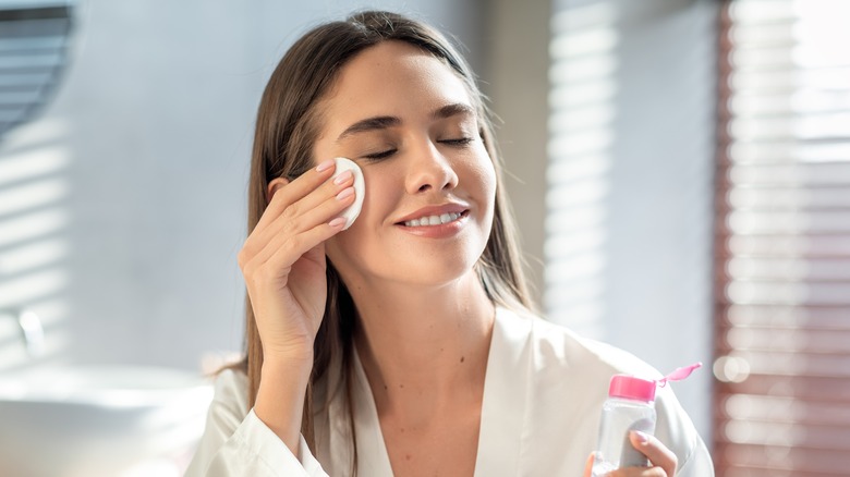 woman cleansing face with cotton pad