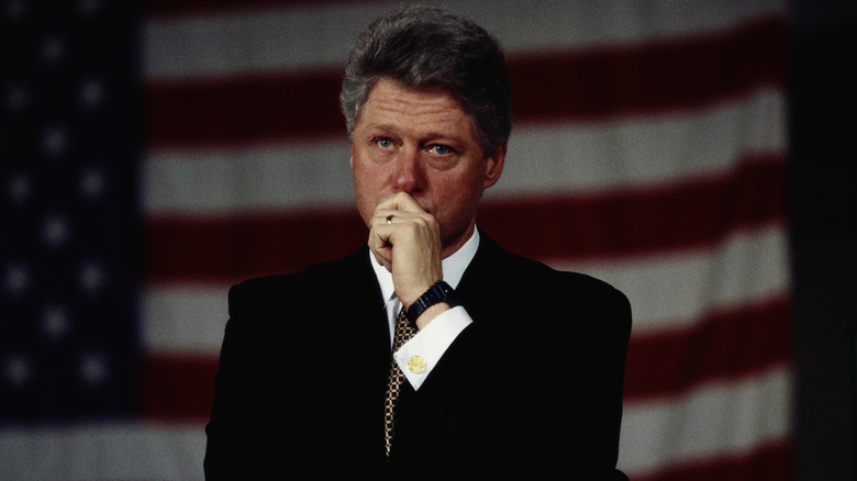 Bill Clinton holding hand to face in front of American flag