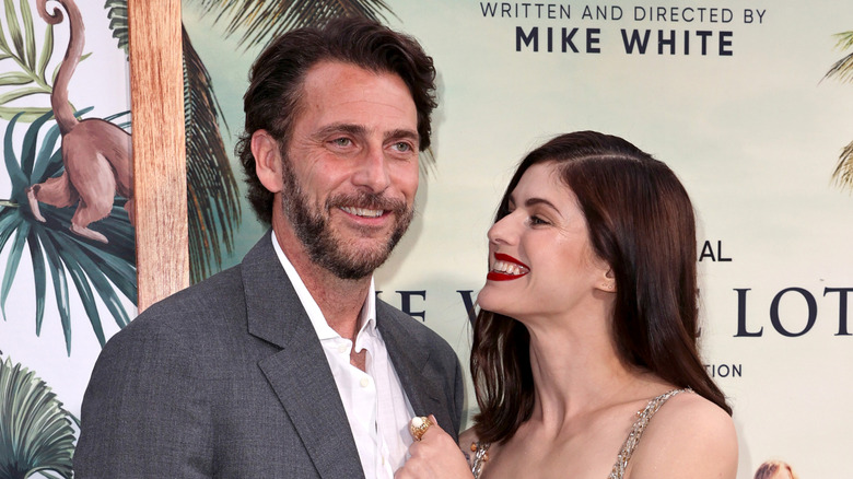 Andrew Form and Alexandra Daddario smiling on "The White Lotus" red carpet