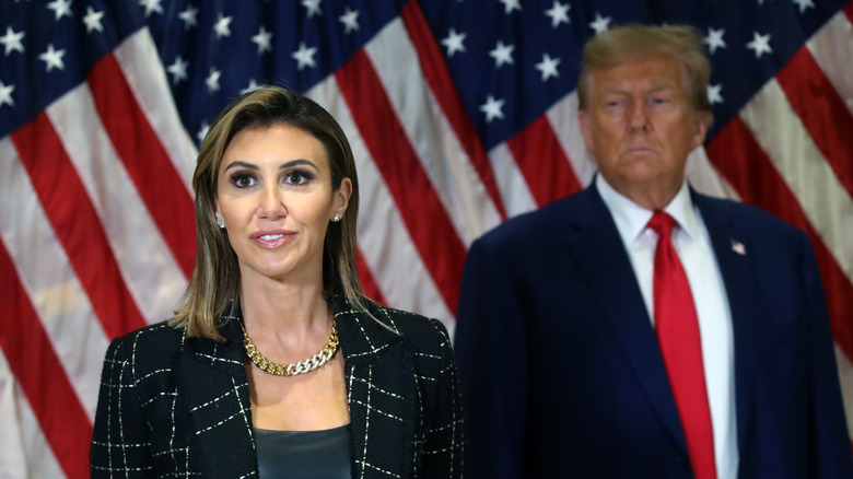 Alina Habba stands near Donald Trump in front of U.S. flags