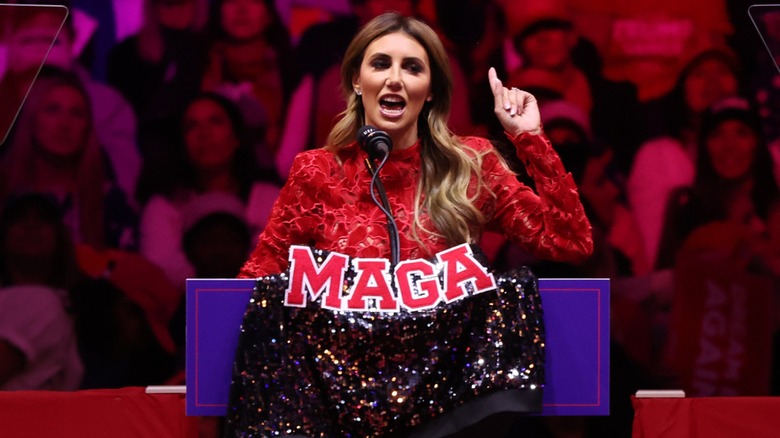 Alina Habba speaking at podium with a sparkly 'MAGA' jacket draped on it