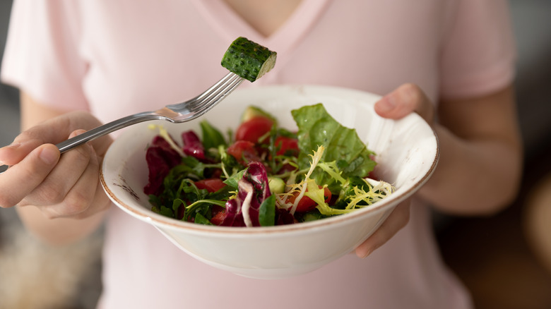 A mom wearing a pink T-shirt eating a bowl of salad