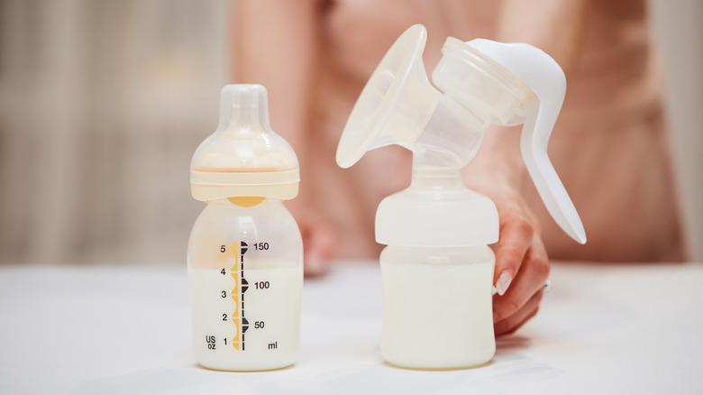 A mom reaching to grab her breast pump that is placed near a bottle of milk