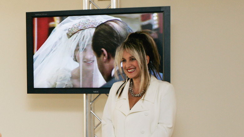 Elizabeth Emanuel smiles in front of a glass case of dresses