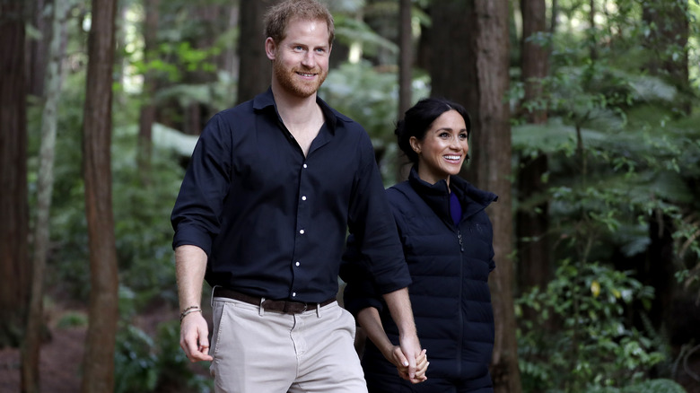 Prince Harry and Meghan Markle walking through forest smiling 