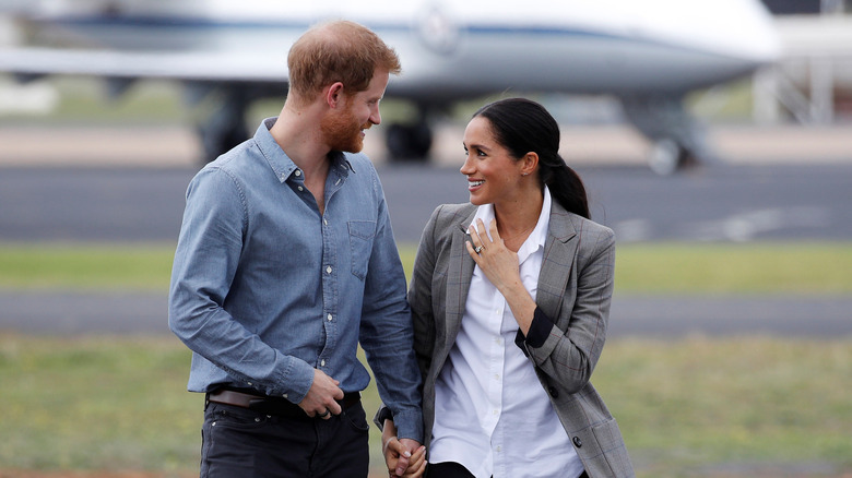 Prince Harry and Meghan Markle holding hands smiling at each other