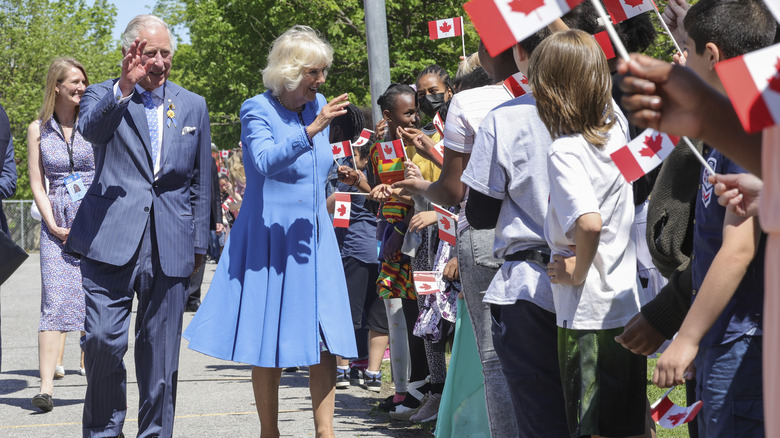 Charles and Camilla greeting people waving Canadian flags