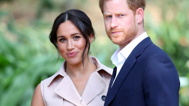 Prince Harry frowning and Meghan Markle smiling at the camera