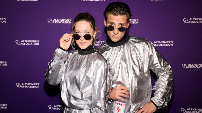 Cassandra Troy and Andrew Walker wearing matching silver outfits and round sunglasses