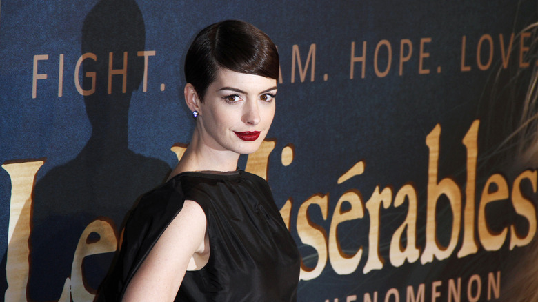 Anne Hathaway posing in front of a "Les Miserables" movie poster