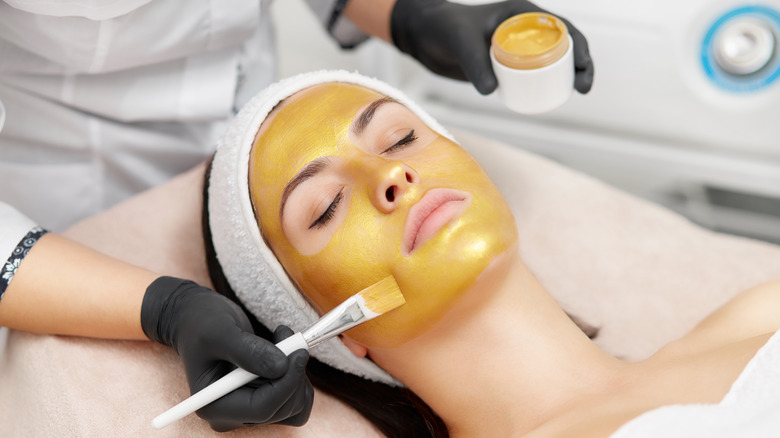 Woman getting gold mask applied to skin