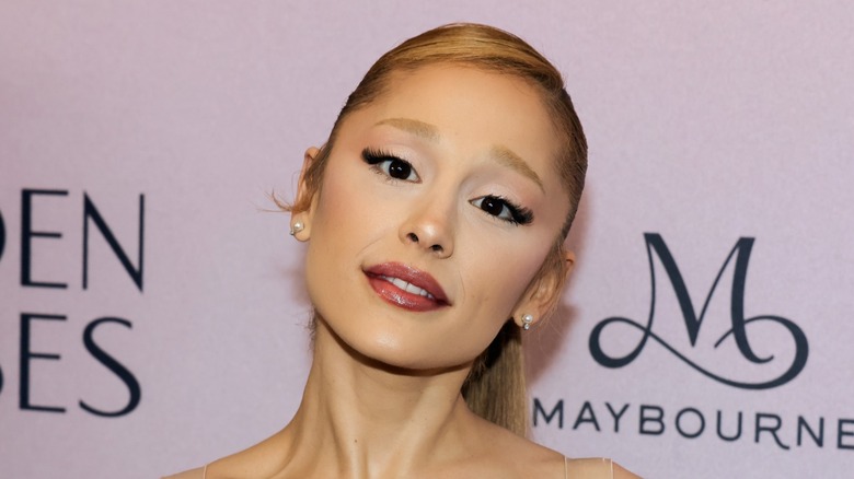 Ariana Grande smiling in dark red lipstick on the red carpet December 2024