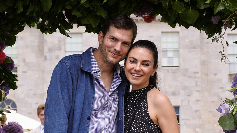 Ashton Kutcher and Mila Kunis smiling under a flower arch