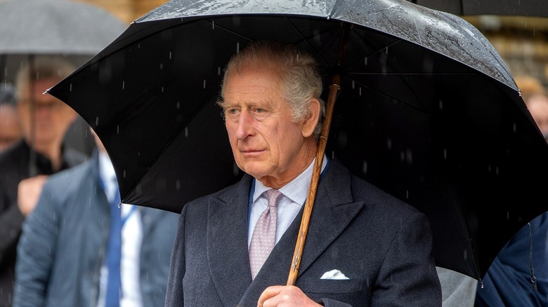 King Charles raining umbrella somber look