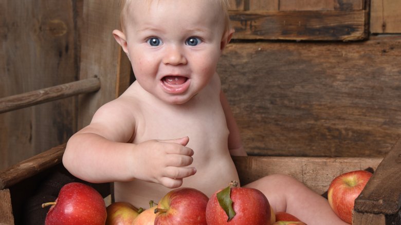 surprised baby sitting in a crate of apples