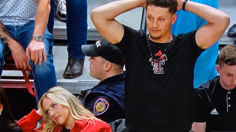 Brittany Mahomes looking bored sitting in bleachers while Patrick looks stressed holding head in hands while standing