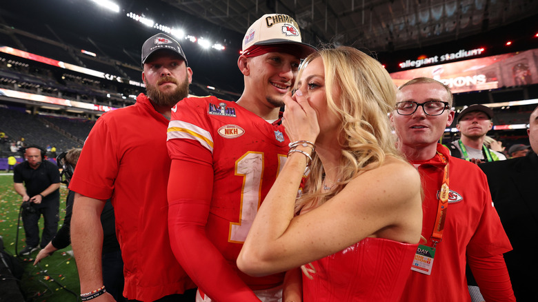 Brittany Mahomes covering her mouth standing next to Patrick Mahomes on football field surrounded by crowds