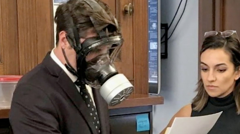 Matt Gaetz in gas mask looking at papers