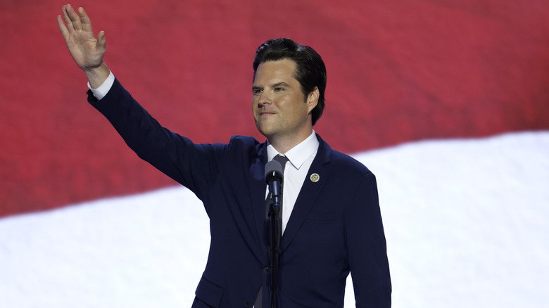 Matt Gaetz raising his hand in the air in front of a microphone