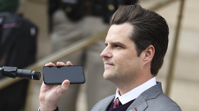 Matt Gaetz holding up a phone in front of a microphone