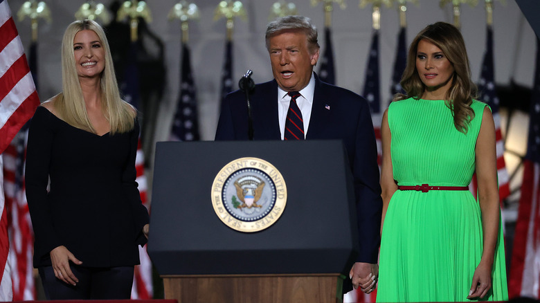 Donald Trump speaking at podium flanked by Melania Trump and Ivanka Trump