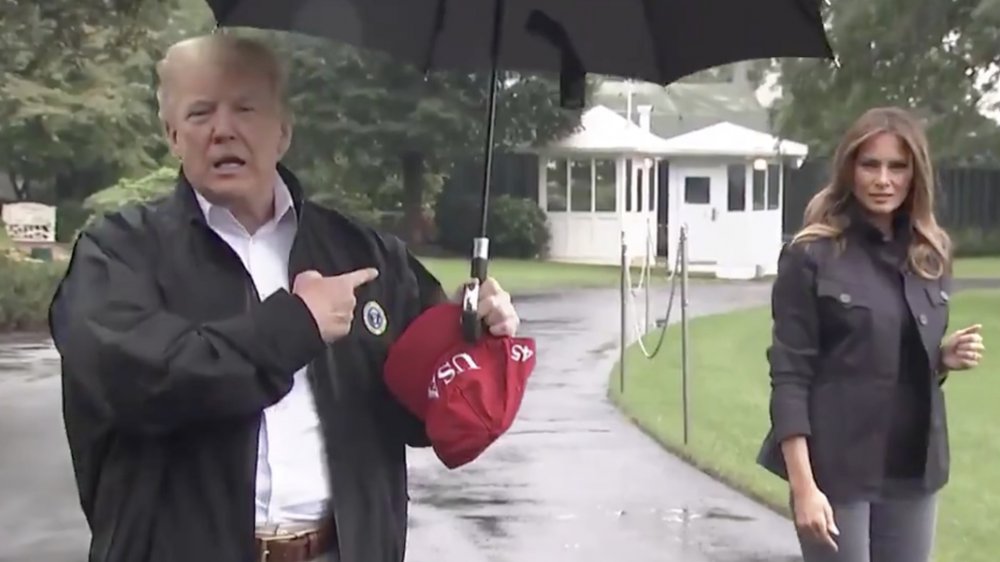 Donald Trump under umbrella pointing at rain-drenched Melania Trump