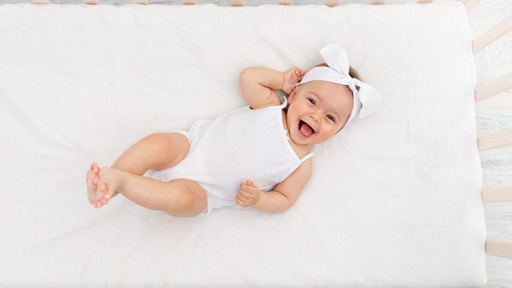 Baby dressed in white clothes lying in crib