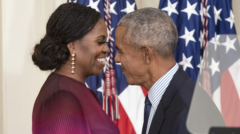 Michelle and Barack Obama smiling and leaning in close to each other