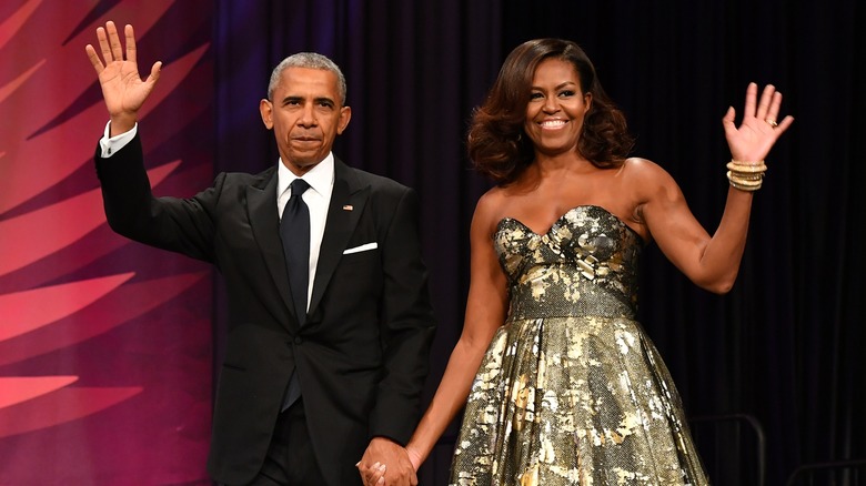 Barack and Michelle Obama in formalwear, holding hands and waving