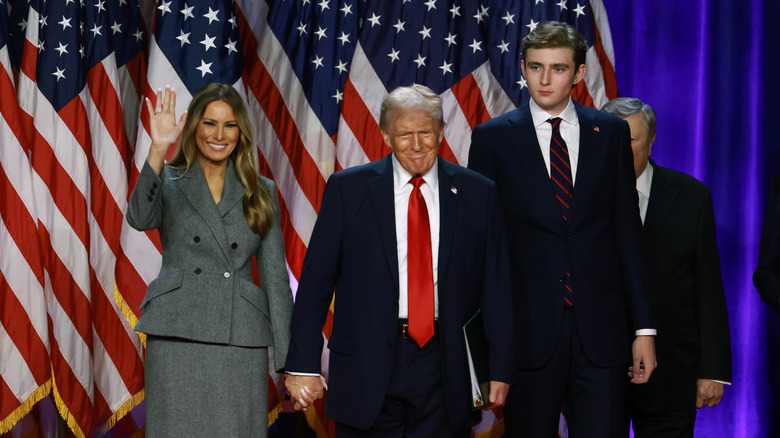 Melania, Donald, and Barron Trump stand side by side in front of American flags