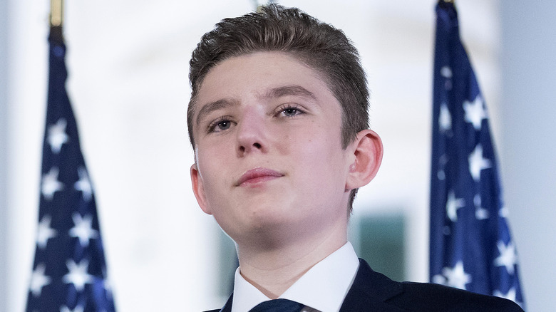 Barron Trump standing in front of two American flags