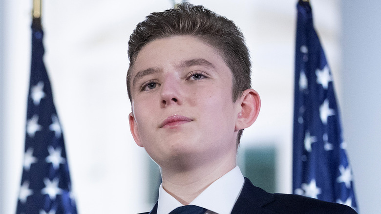 Barron Trump standing in front of two American flags