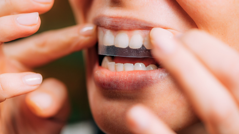 Woman applying teeth whitening strip