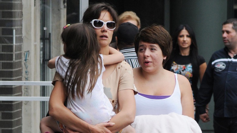 Bella Cruise walking with Katie Holmes who holds Suri