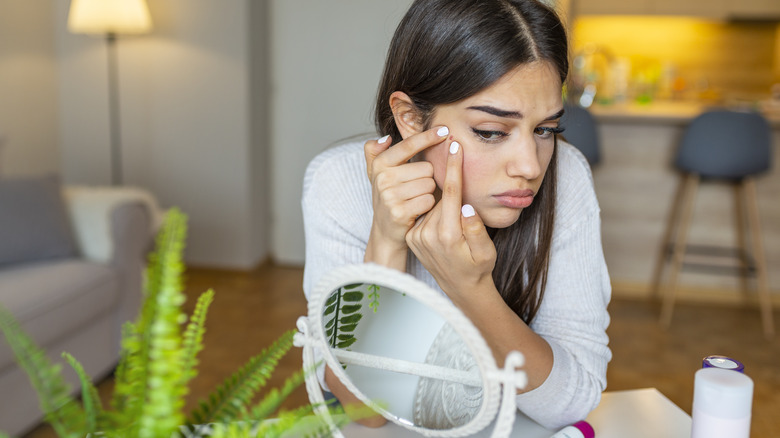 Woman picking at her face in mirror